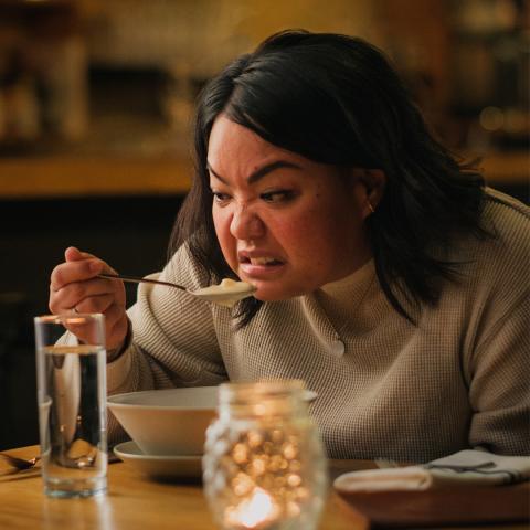 Image of person in a restaurant eating soup with a distasteful look on their face.